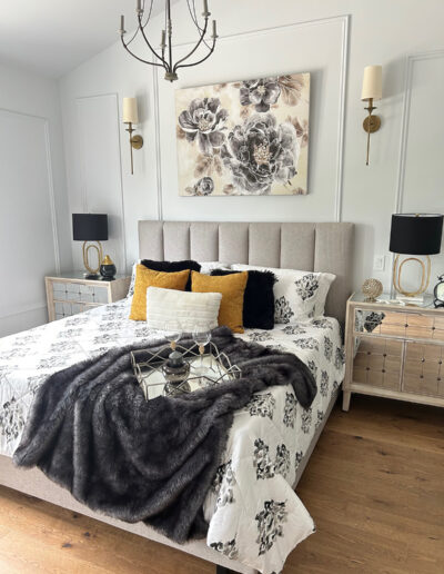 Bedroom staged for real estate listing with a padded, grey headboard, white bedding, gold accent pillows, and a dark grey throw blanket.
